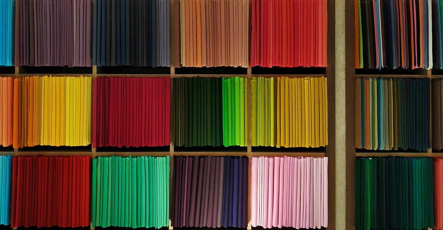 Folded colorful textiles arranged in neat stacks on wooden shelves.