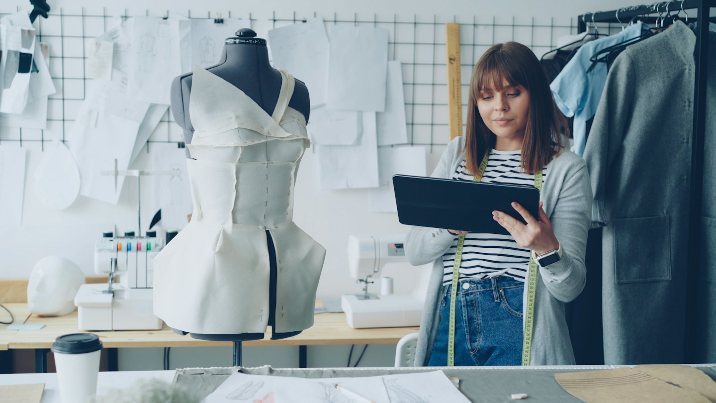 Fashion designer reviewing digital patterns on a tablet in her studio.